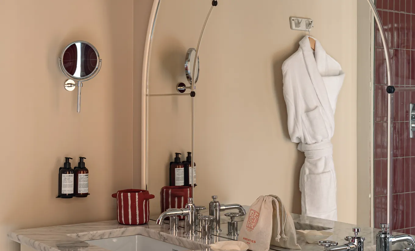 Experimental Group hotel bathroom vanity with vintage arched mirror, marble countertop, and luxury toiletries display