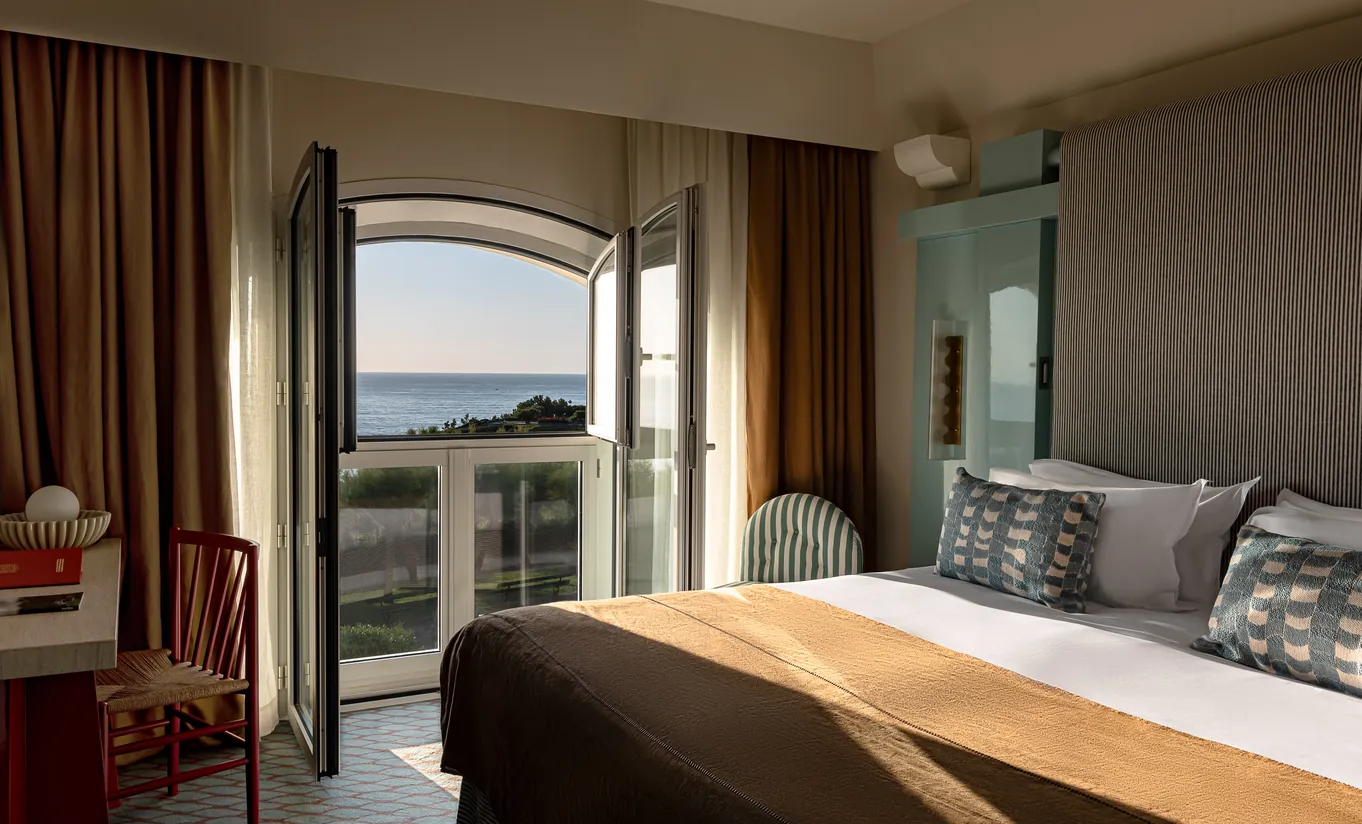 Elegant bedroom with warm golden drapery, arched window and stunning sea view at Experimental Group.