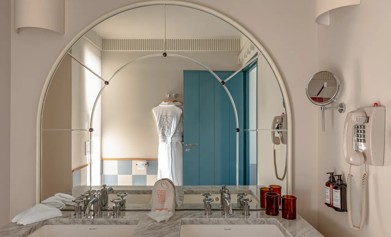 Regina Experimental hotel bathroom with large arched mirror, marble sink, vintage fixtures, and teal blue accent wall