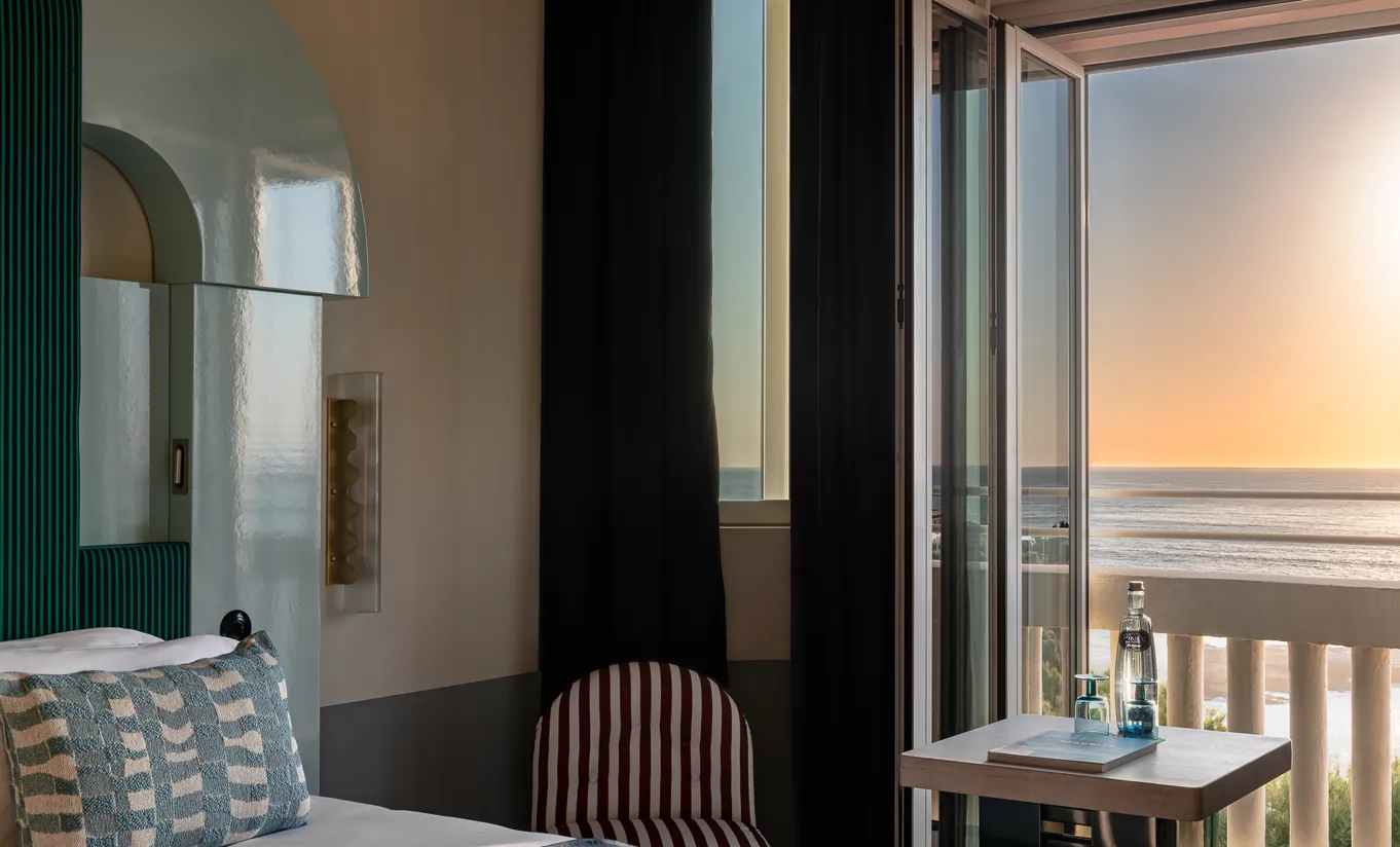 Regina Experimental hotel room with dining table, chairs, and stunning golden sunset view over the ocean from private balcony