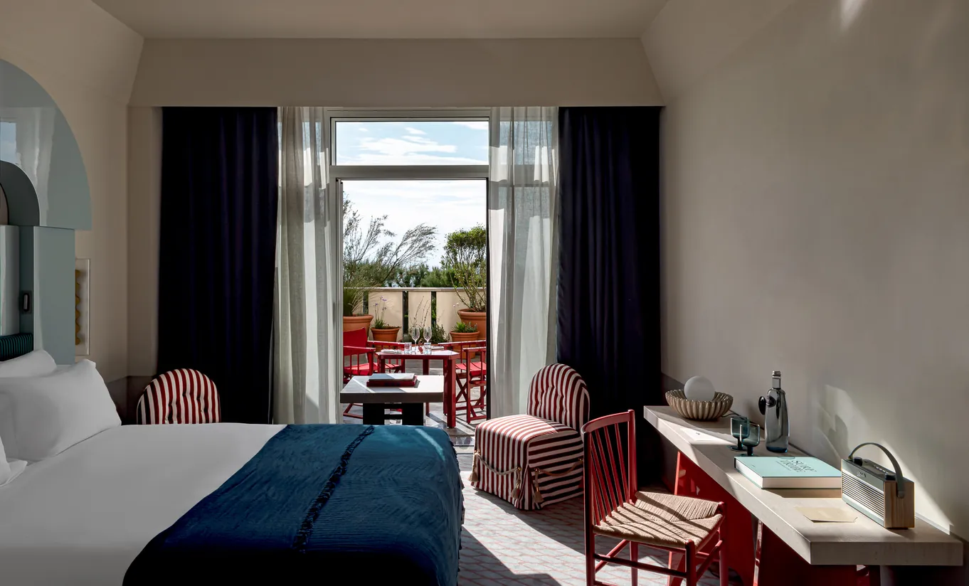 Experimental Paris hotel superior room with blue bedding, red accents, and open French doors leading to a furnished private terrace