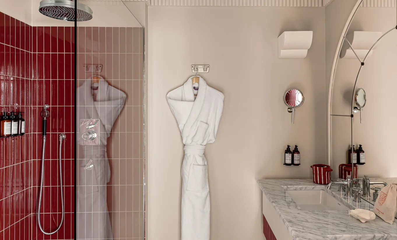 Experimental Paris hotel bathroom with red mosaic tiled shower, white bathrobe on hook, and marble sink vanity