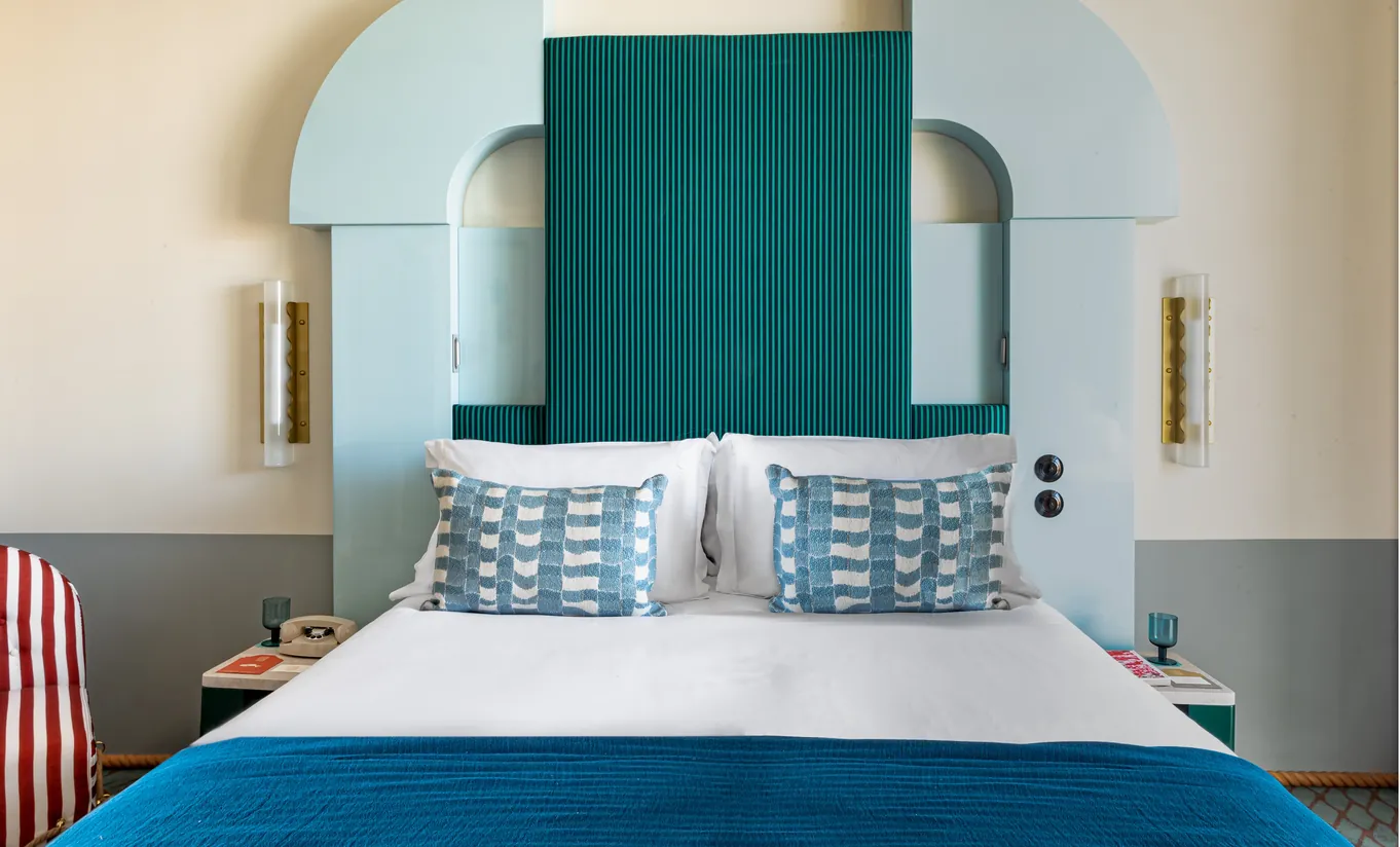 Regina Experimental hotel bedroom with statement teal green arched headboard, geometric patterned cushions, and soft white bedding