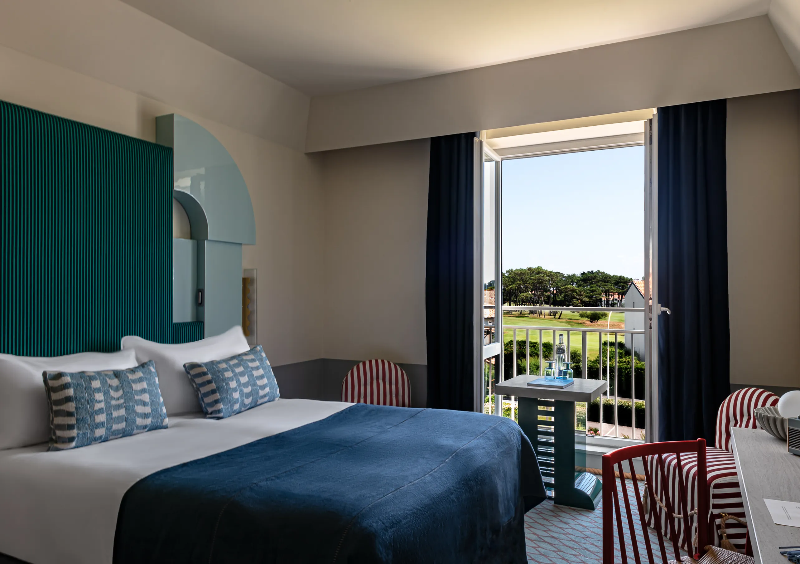 Regina Experimental hotel superior room with blue bedding, teal accent wall, dark curtains, and balcony door open to golf course view.