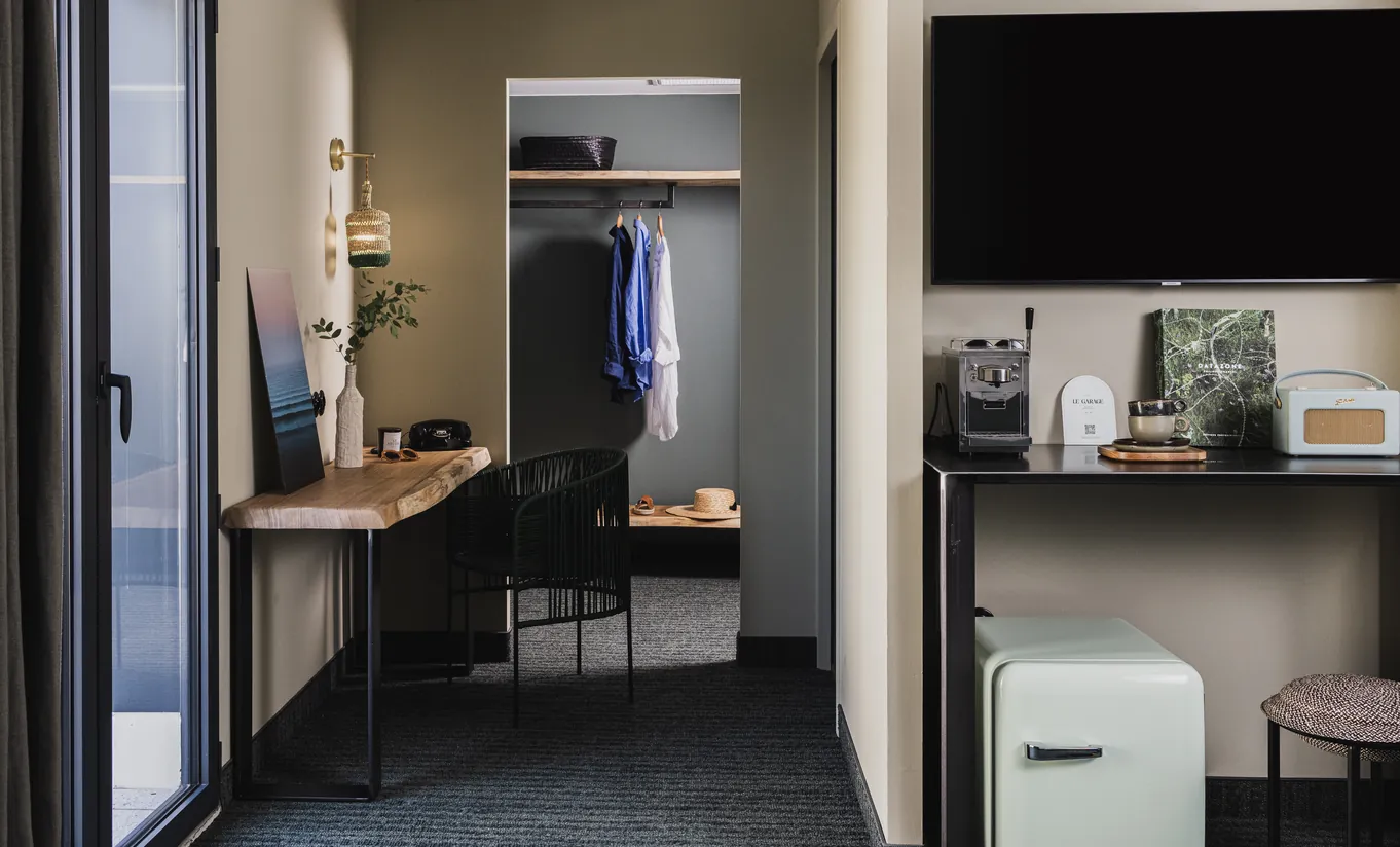 Le Garage Biarritz Experimental hotel room with open wardrobe, wooden desk, flat screen TV, and industrial-style dark wall finishes