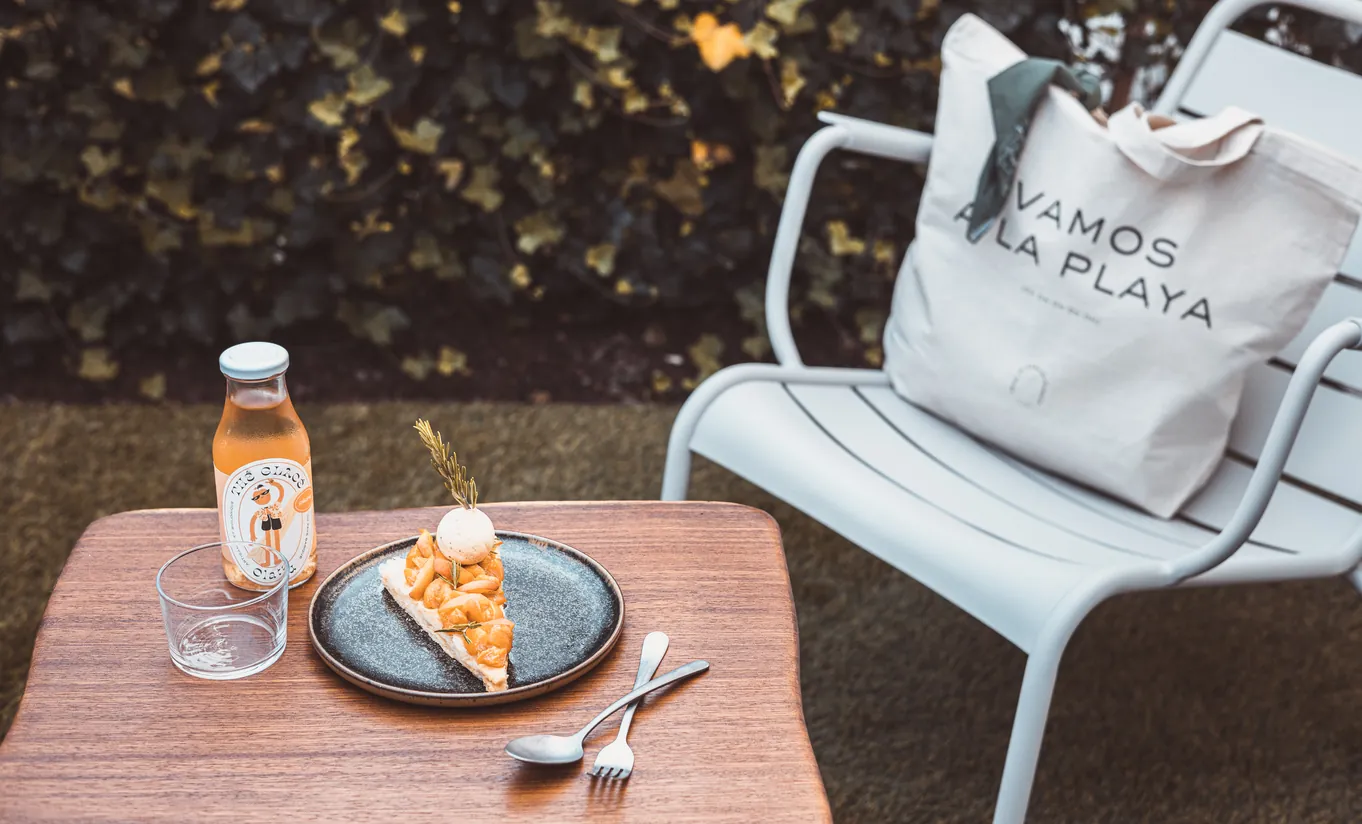 Le Garage Biarritz Experimental hotel outdoor terrace with metal bistro chair, breakfast plate, juice bottle, and tote bag on wooden table