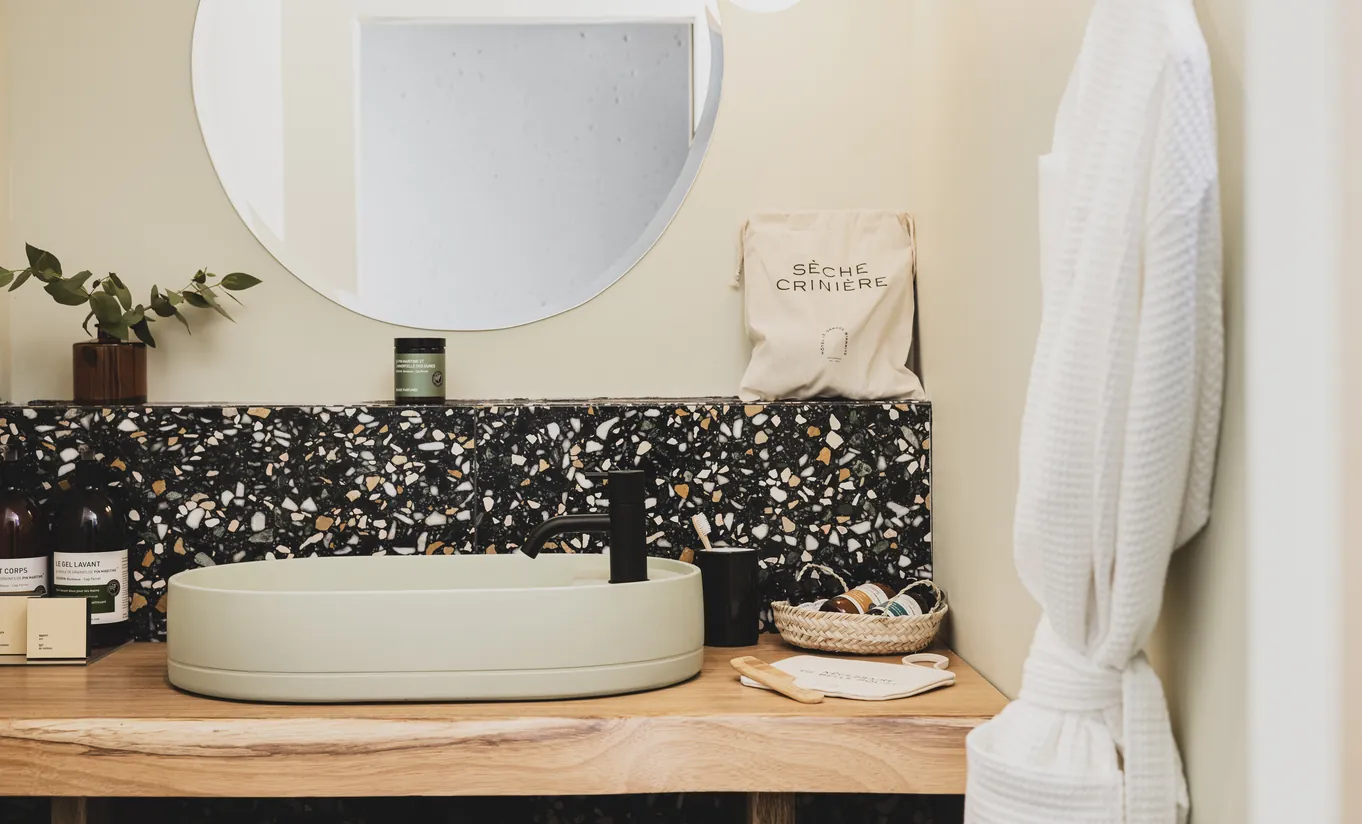 Le Garage Biarritz Experimental hotel bathroom with round white vessel sink, dark terrazzo splashback, and warm wood vanity countertop