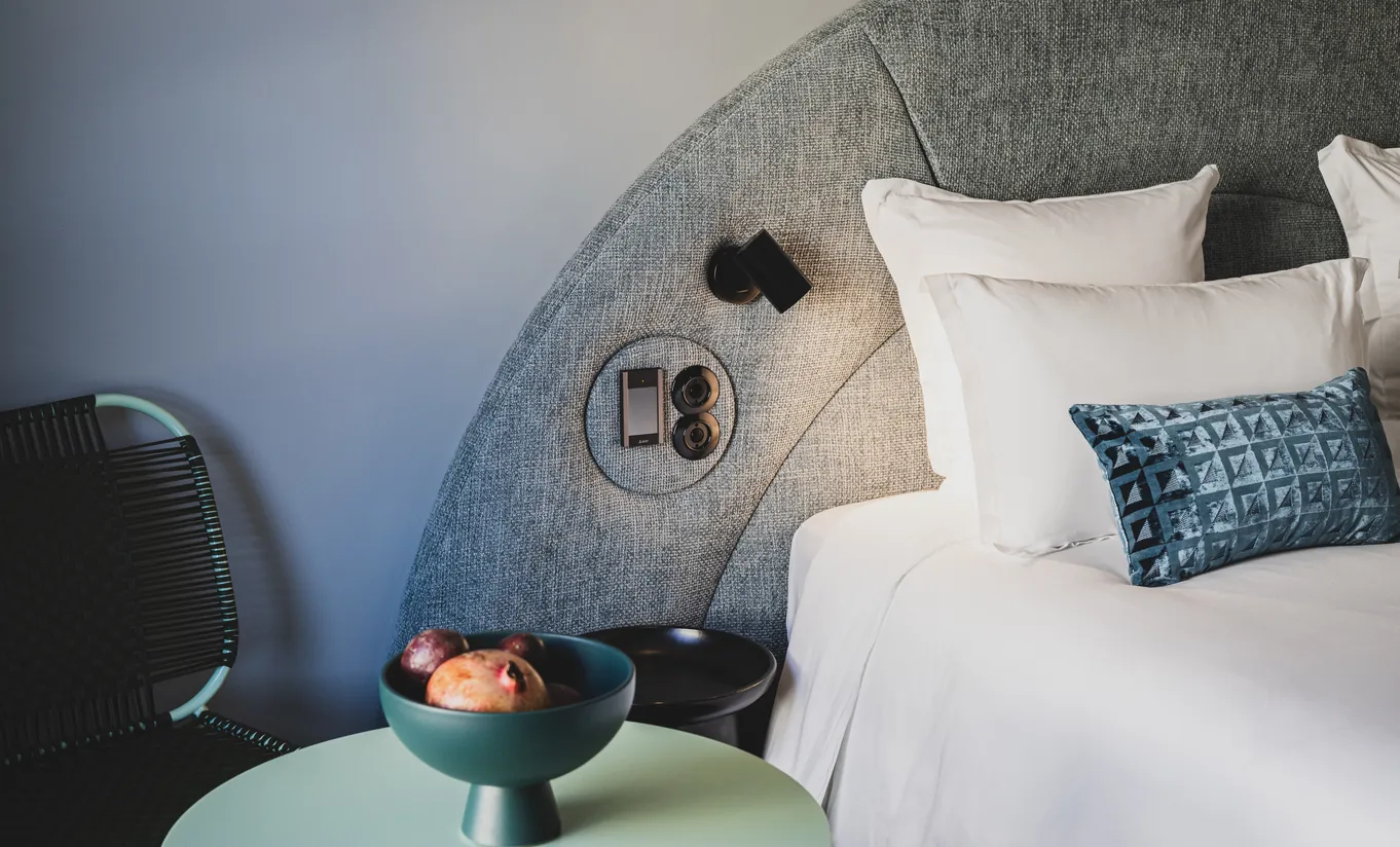 Le Garage Biarritz Experimental hotel bedroom with curved grey headboard, white bedding, blue accent cushions, and warm ambient lighting