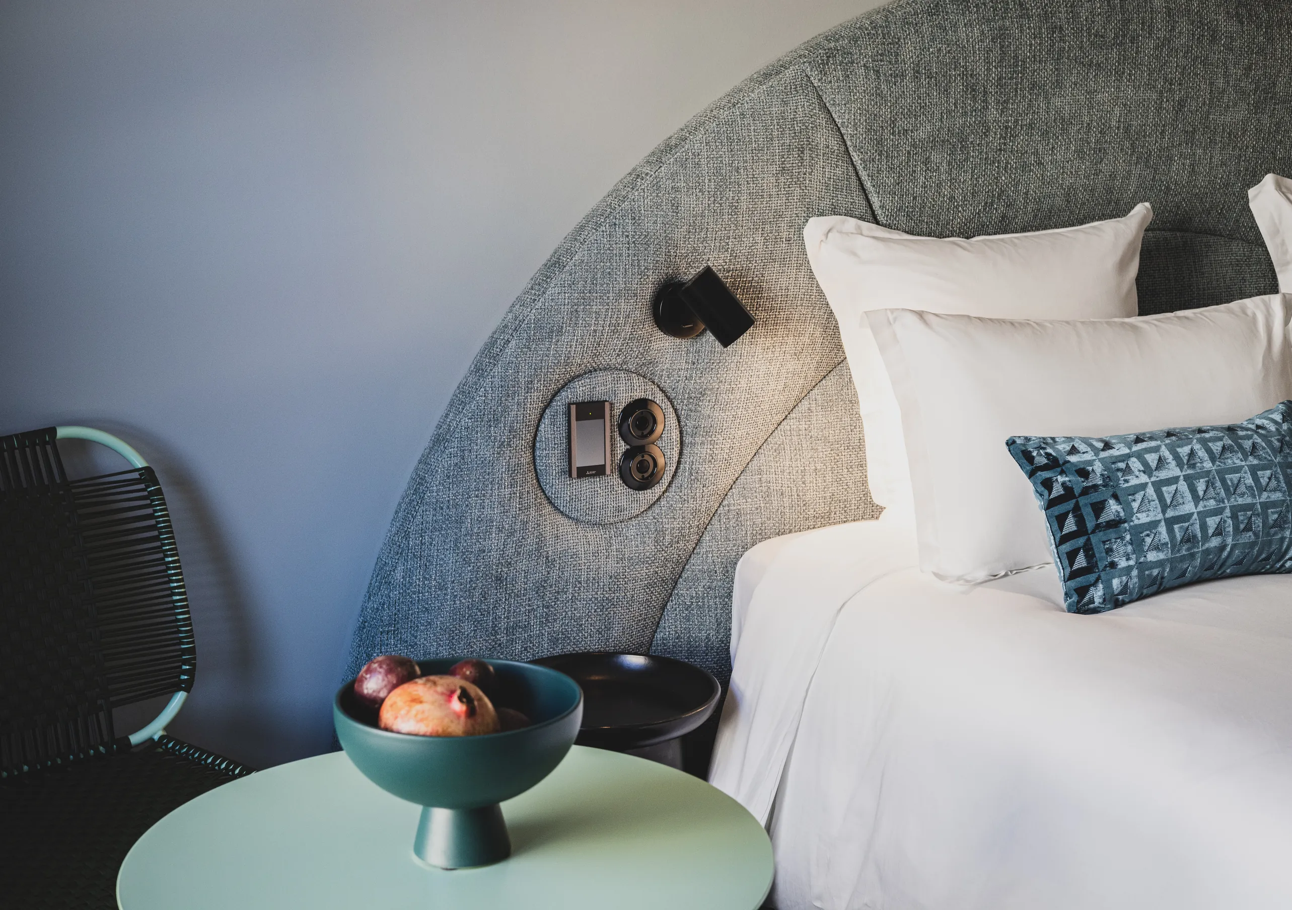Le Garage Biarritz Experimental hotel bedroom with curved grey headboard, white bedding, blue accent cushions, and warm ambient lighting.