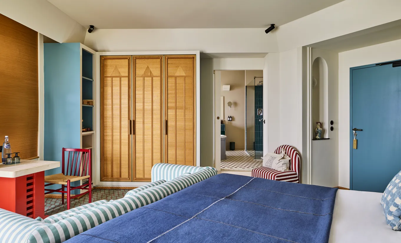 Regina Experimental Biarritz hotel bedroom with blue striped bedding, wooden slatted wardrobe doors, and colorful blue accent wall