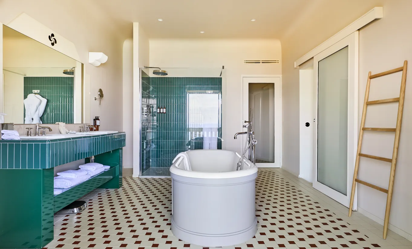 egina Experimental Biarritz hotel spacious bathroom with freestanding bathtub, teal green walls, black and white patterned floor tiles, and walk-in shower