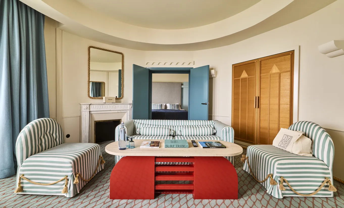 Experimental Group hotel suite living room with two grey armchairs, red coffee table, fireplace, and teal blue accent wall
