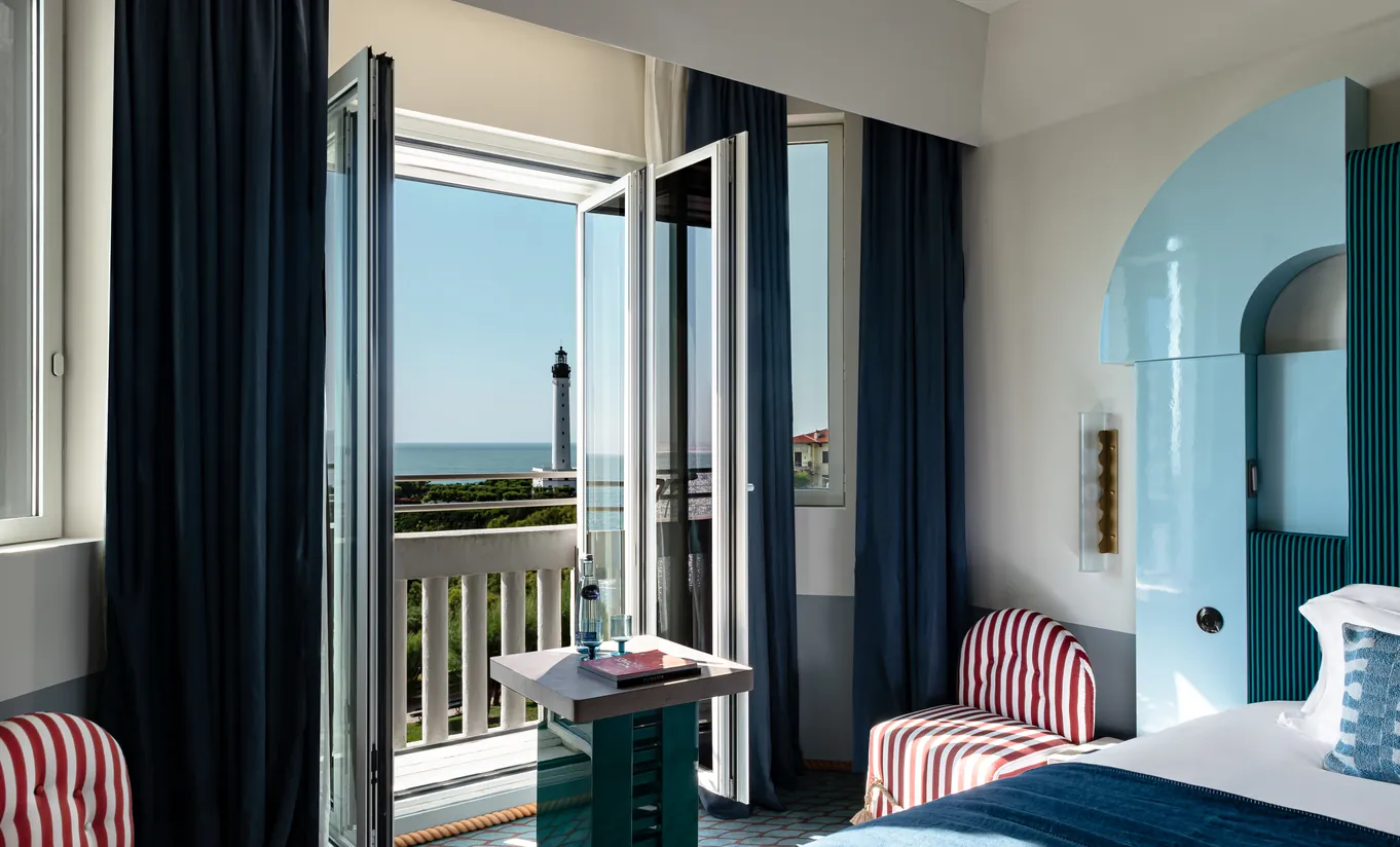 Regina Experimental Biarritz hotel bedroom with navy blue curtains, white bedding, and direct sea view through open glass doors