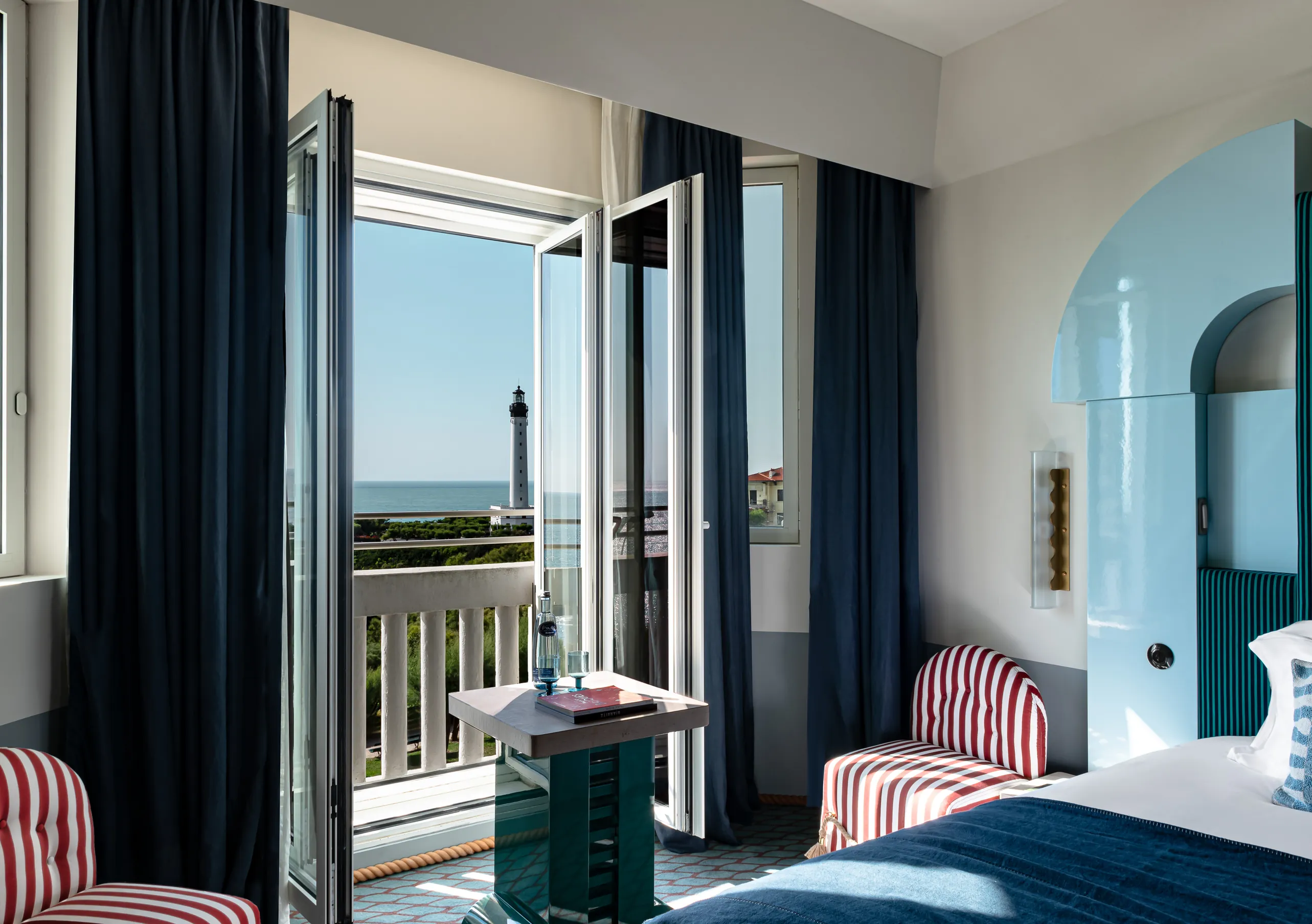 Regina Experimental Biarritz hotel bedroom with navy blue curtains, white bedding, and direct sea view through open glass doors.