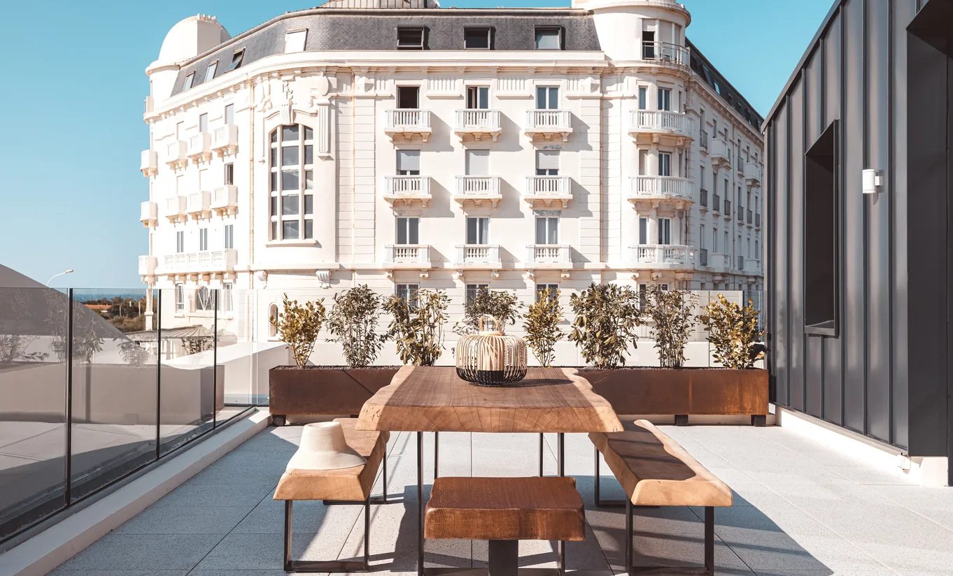Experimental Group hotel rooftop terrace with wooden furniture and sweeping view of a classic Haussmann Parisian facade