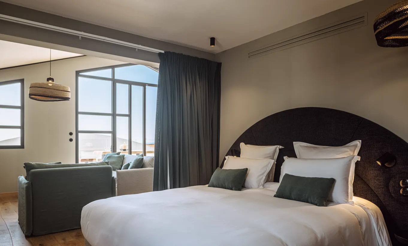 Experimental Group hotel moody bedroom with oversized white pillows, dark walls and steel-framed window letting in natural light