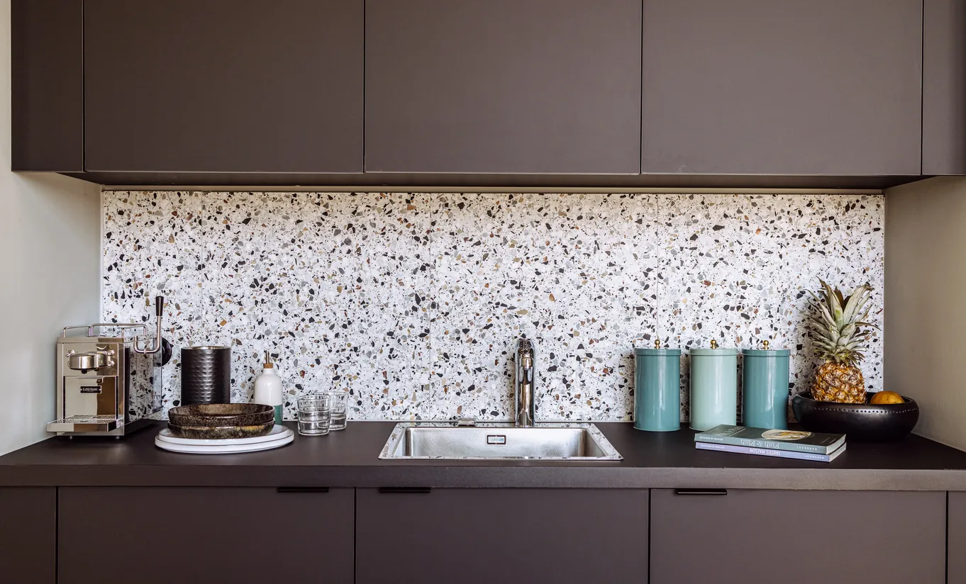 Experimental Group hotel modern kitchen area with terrazzo splashback, dark cabinetry and curated countertop accessories
