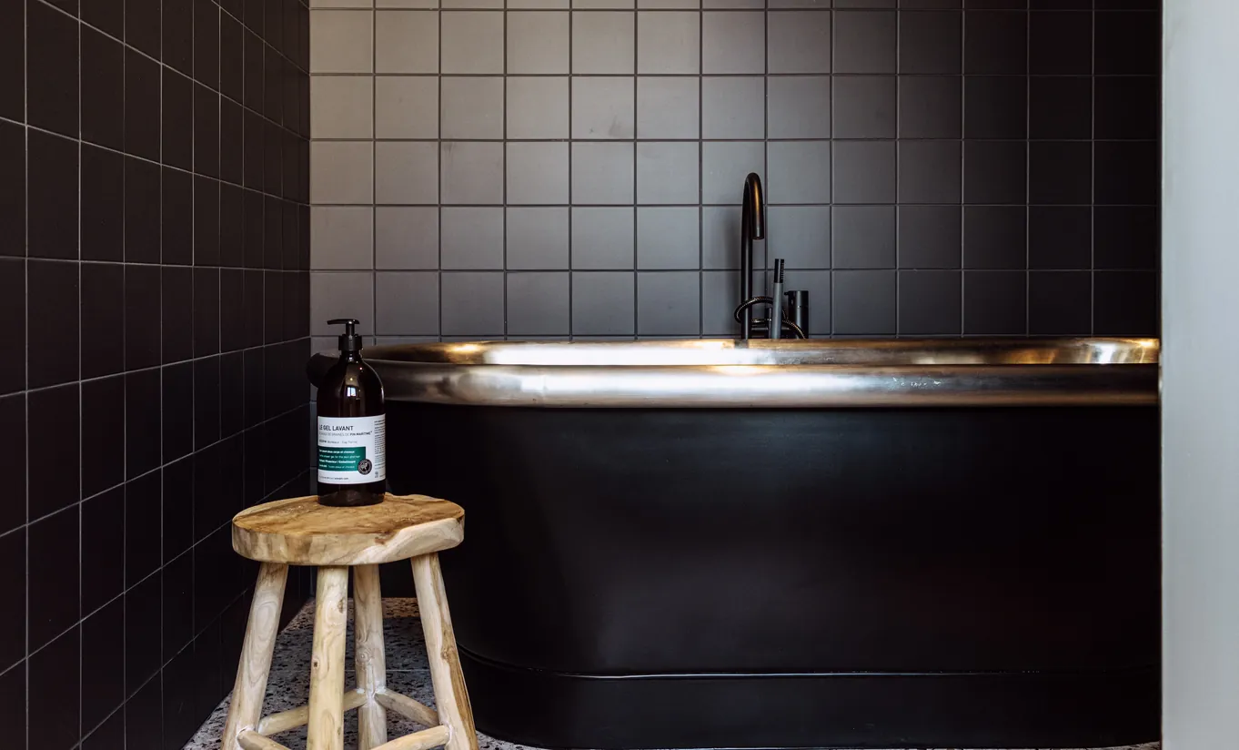 Experimental Group hotel sleek black tiled kitchenette with brass countertop and wooden bar stool