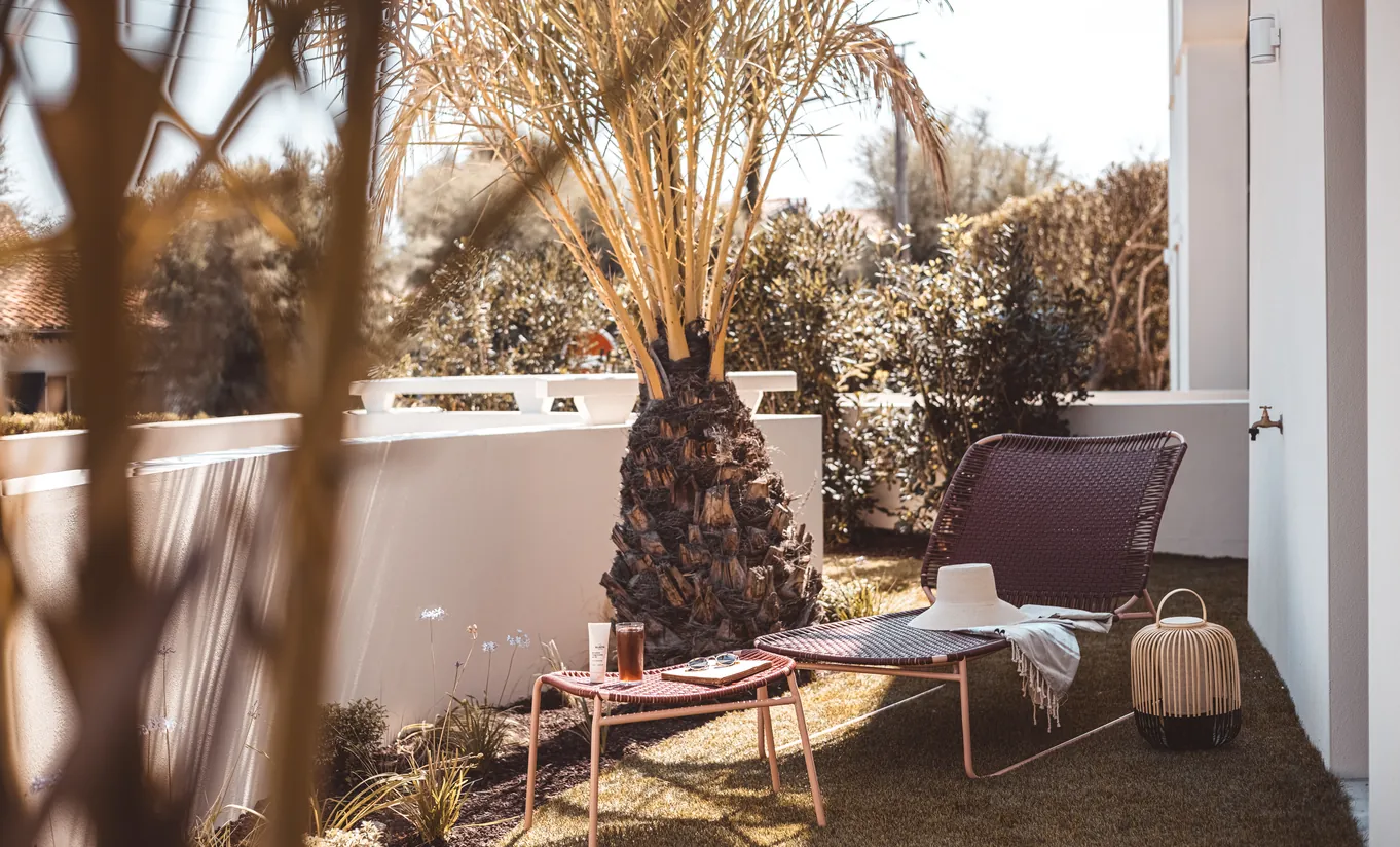 Experimental Group hotel private outdoor terrace with freestanding bathtub, wicker chairs, tropical plants, and whitewashed stone wall