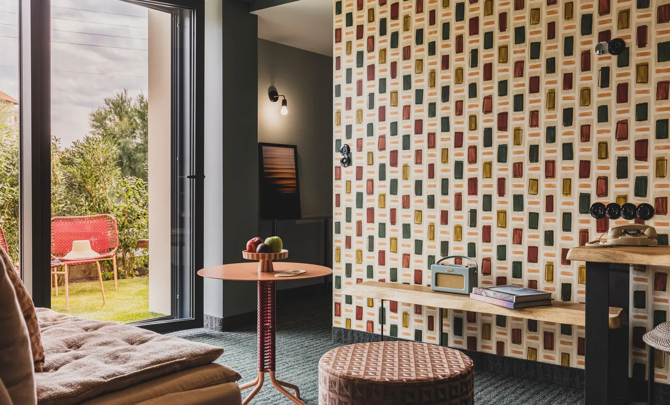 Experimental Group hotel lounge area with geometric black and white patterned wallpaper, round table, pink chairs, and dark green accent wall