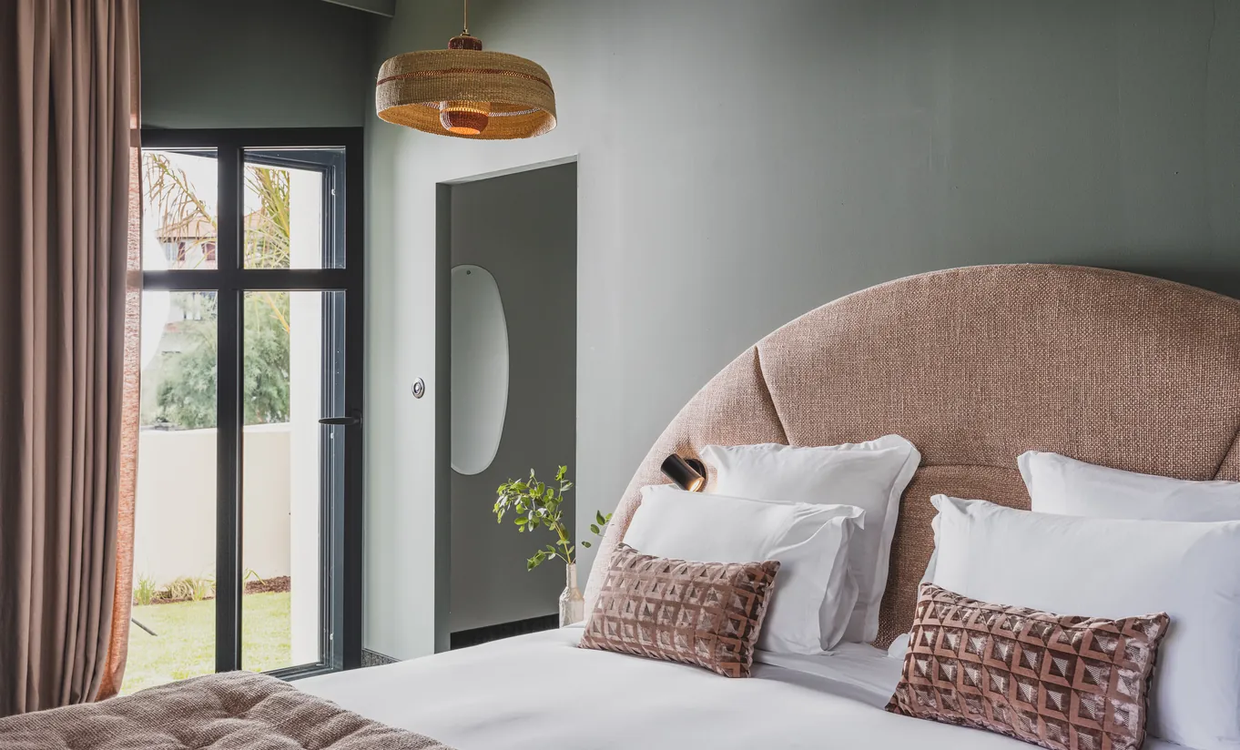 Experimental Group hotel bedroom with oversized blush pink rounded headboard, white bedding, pink cushions, and soft grey walls