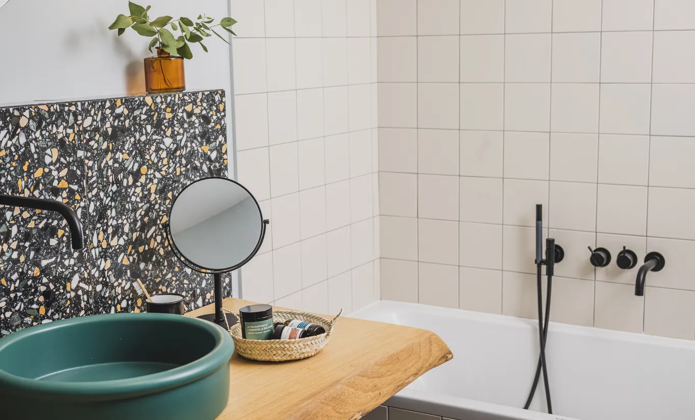 Le Garage Biarritz Experimental hotel bathroom with deep green round vessel sink, yellow wood vanity, mosaic splashback, and black wall-mounted faucet