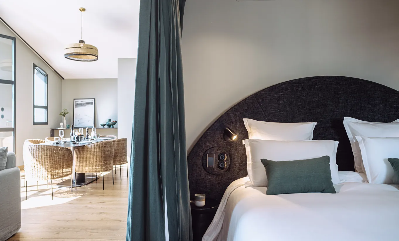 Experimental Group hotel cozy bedroom with dark teal headboard, white bedding and open view to a bright living area