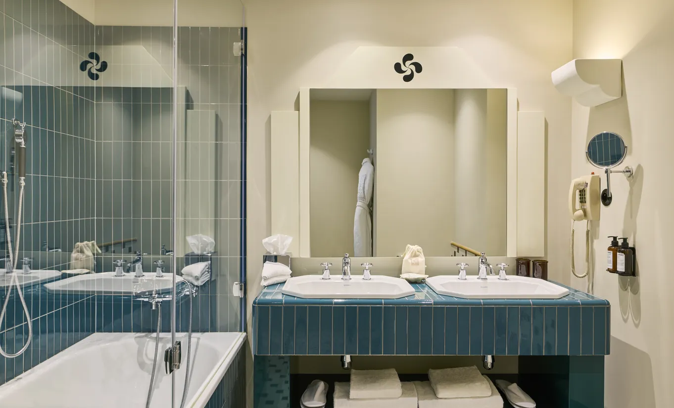 Experimental Group hotel bathroom with teal double vanity, large mirror, glass shower enclosure, and brushed silver fixtures