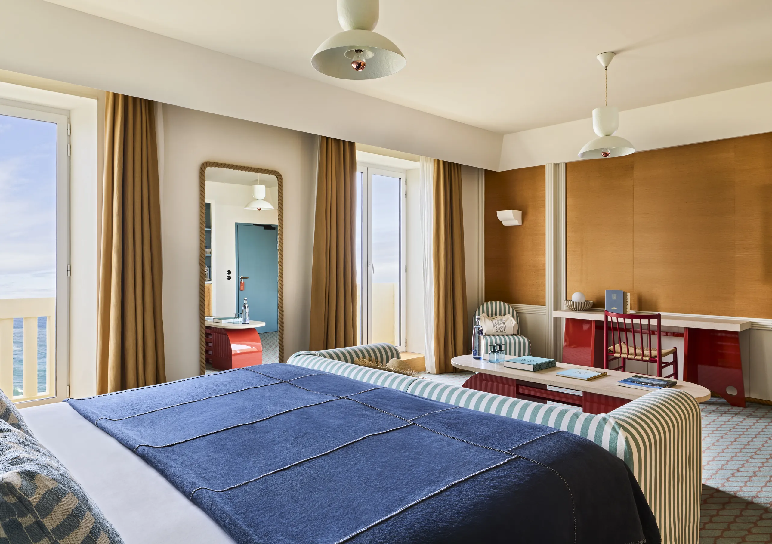 Experimental Group hotel suite with king bed, warm wood paneling, orange curtains, and open view into a bright living area.