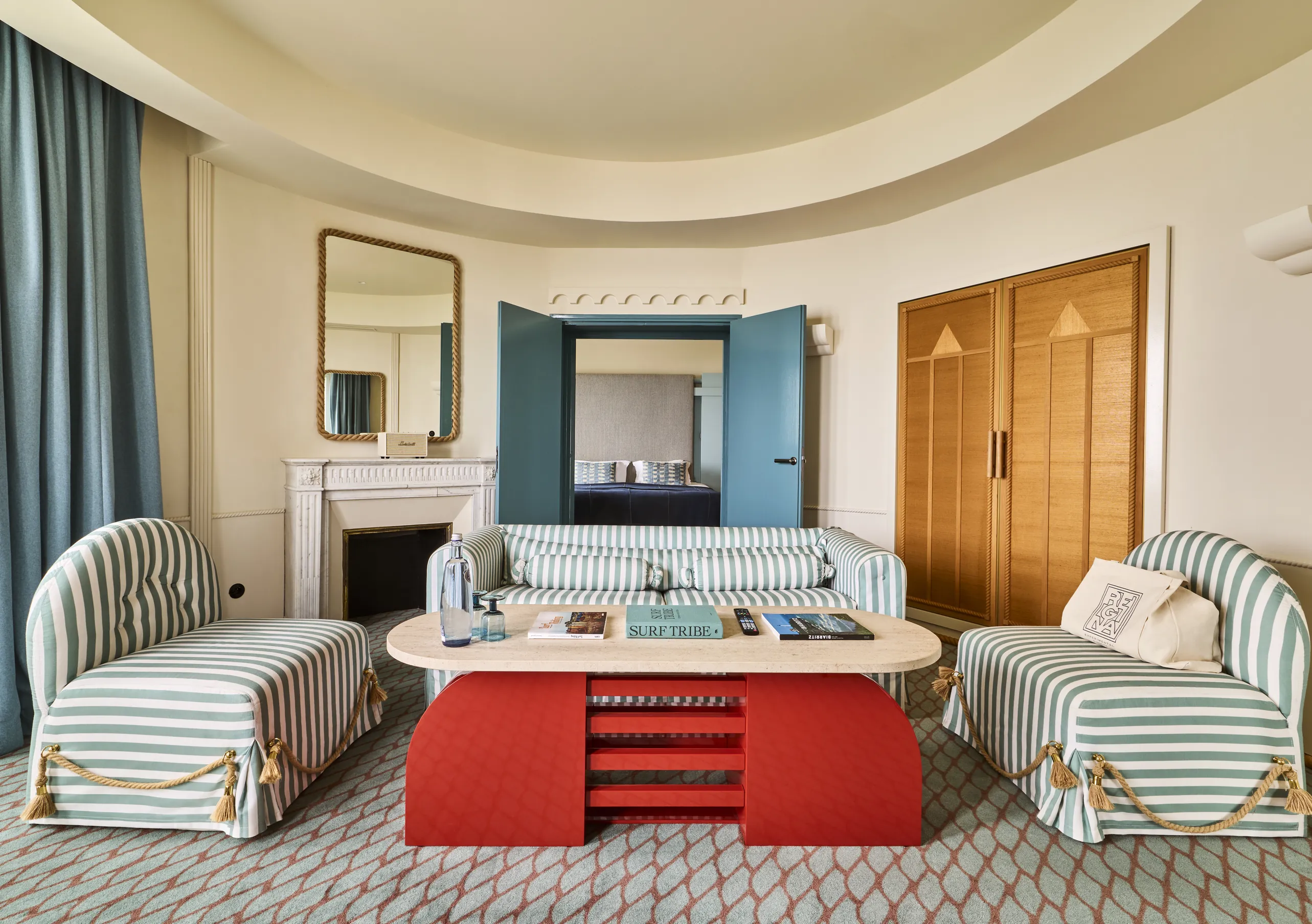 Experimental Group hotel suite living room with two grey armchairs, red coffee table, fireplace, and teal blue accent wall.