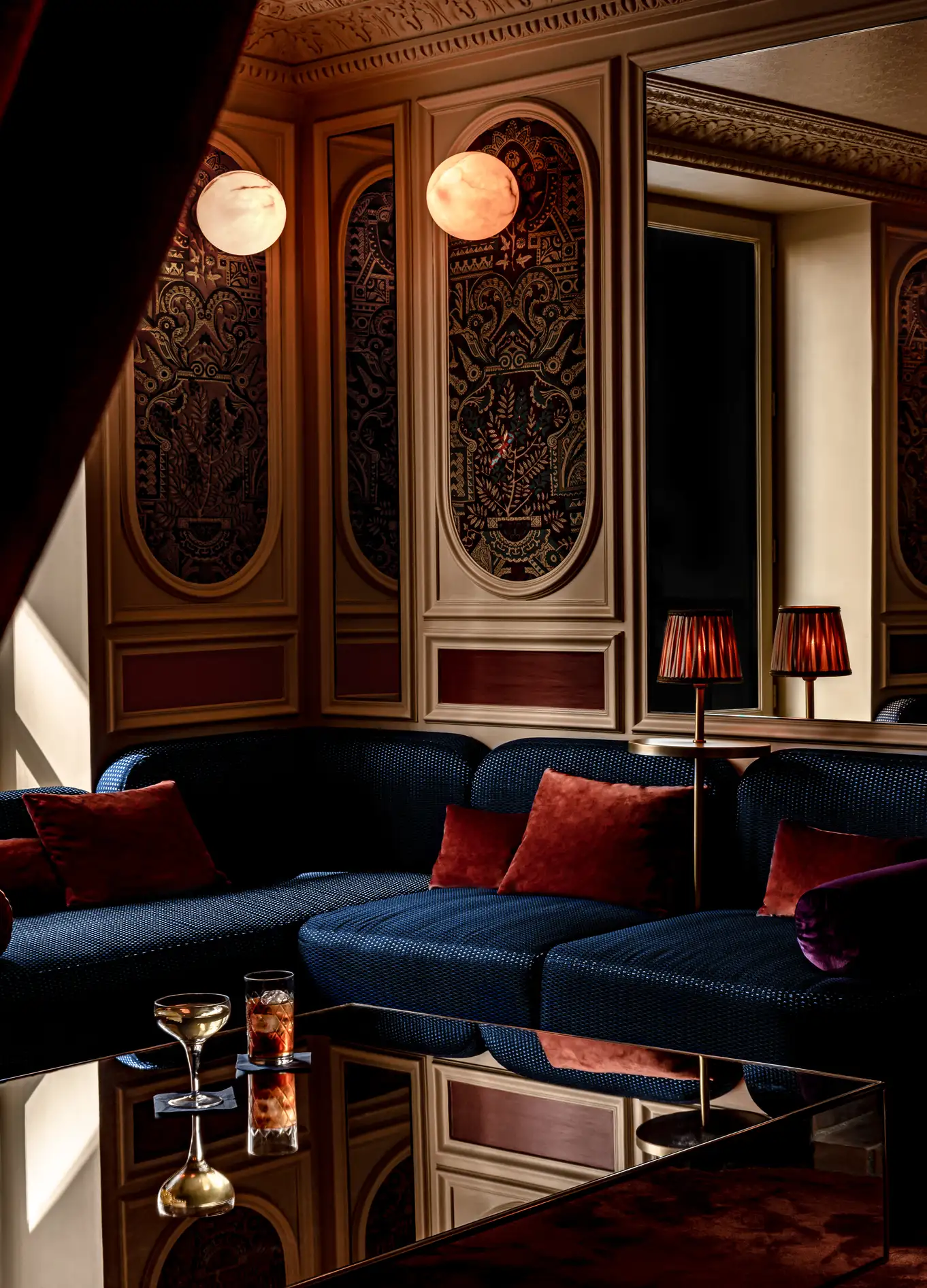 A cozy lounge area with deep blue sofas, red cushions, and dim lighting, creating a sophisticated atmosphere.
