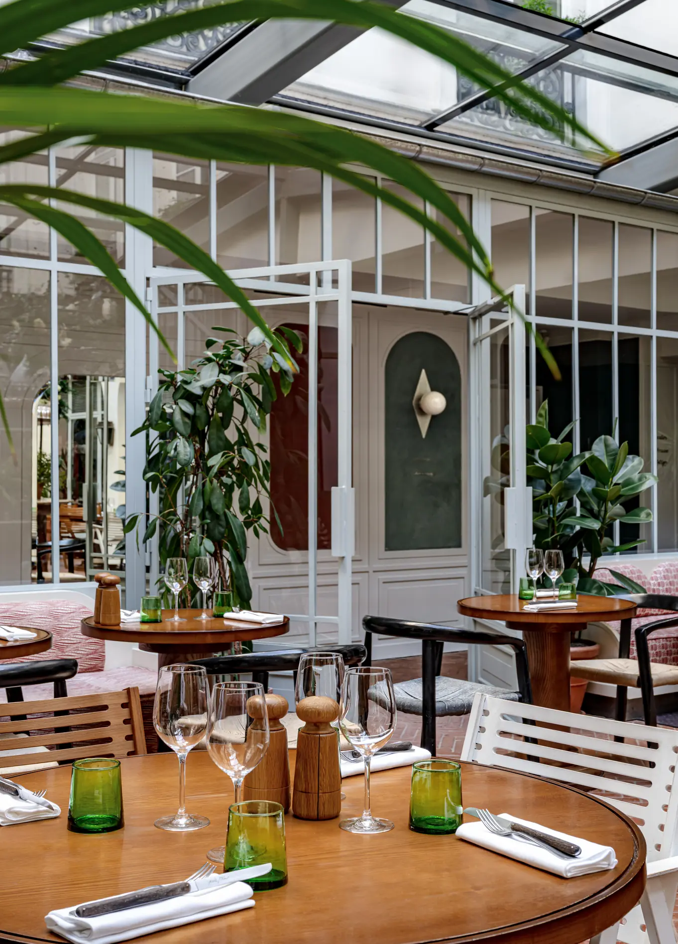 Bright dining room with glass roof, wooden tables and plants at Restaurant des Grands Boulevards, Paris