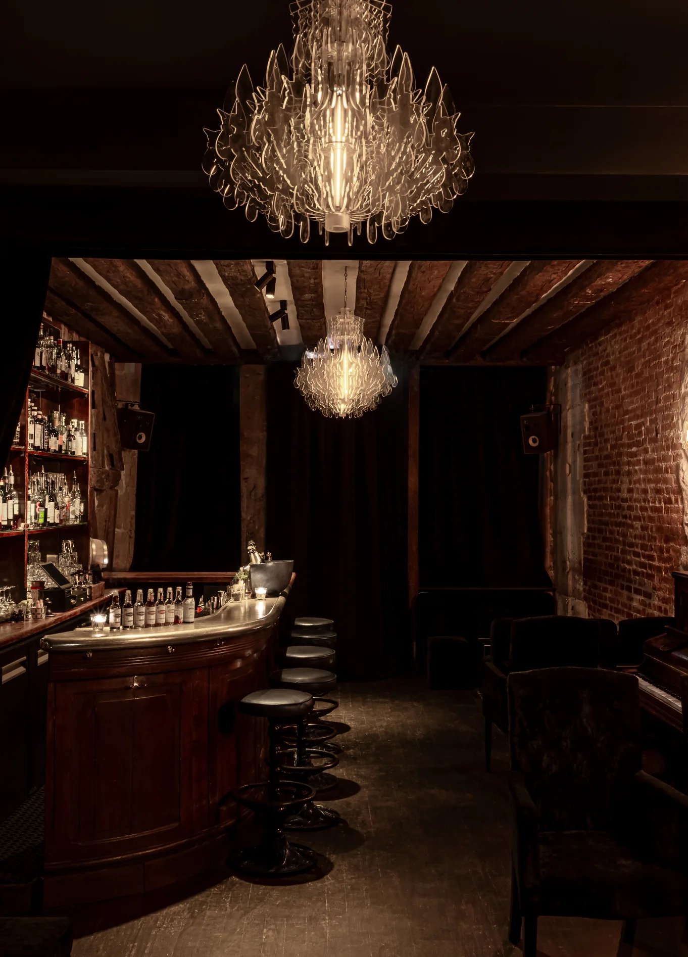 Cozy atmosphere of the Experimental Cocktail Club, showcasing a wooden bar counter, stools, and a decorative chandelier hanging from the ceiling.