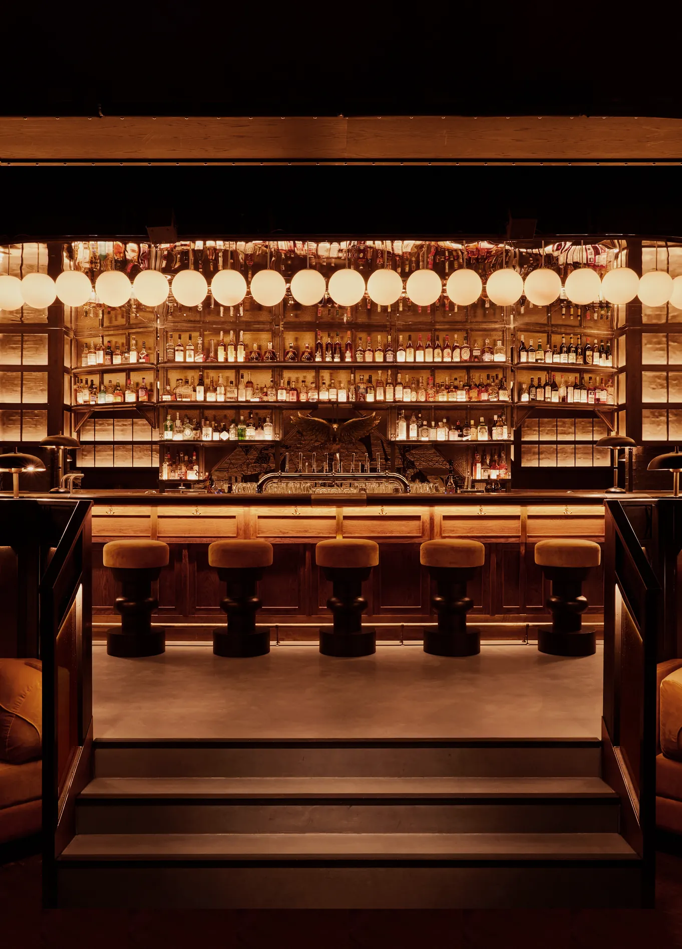 View of the interior of a stylish bar by the Experimental Group, featuring a backlit counter, bar stools, and a cozy lounge area.
