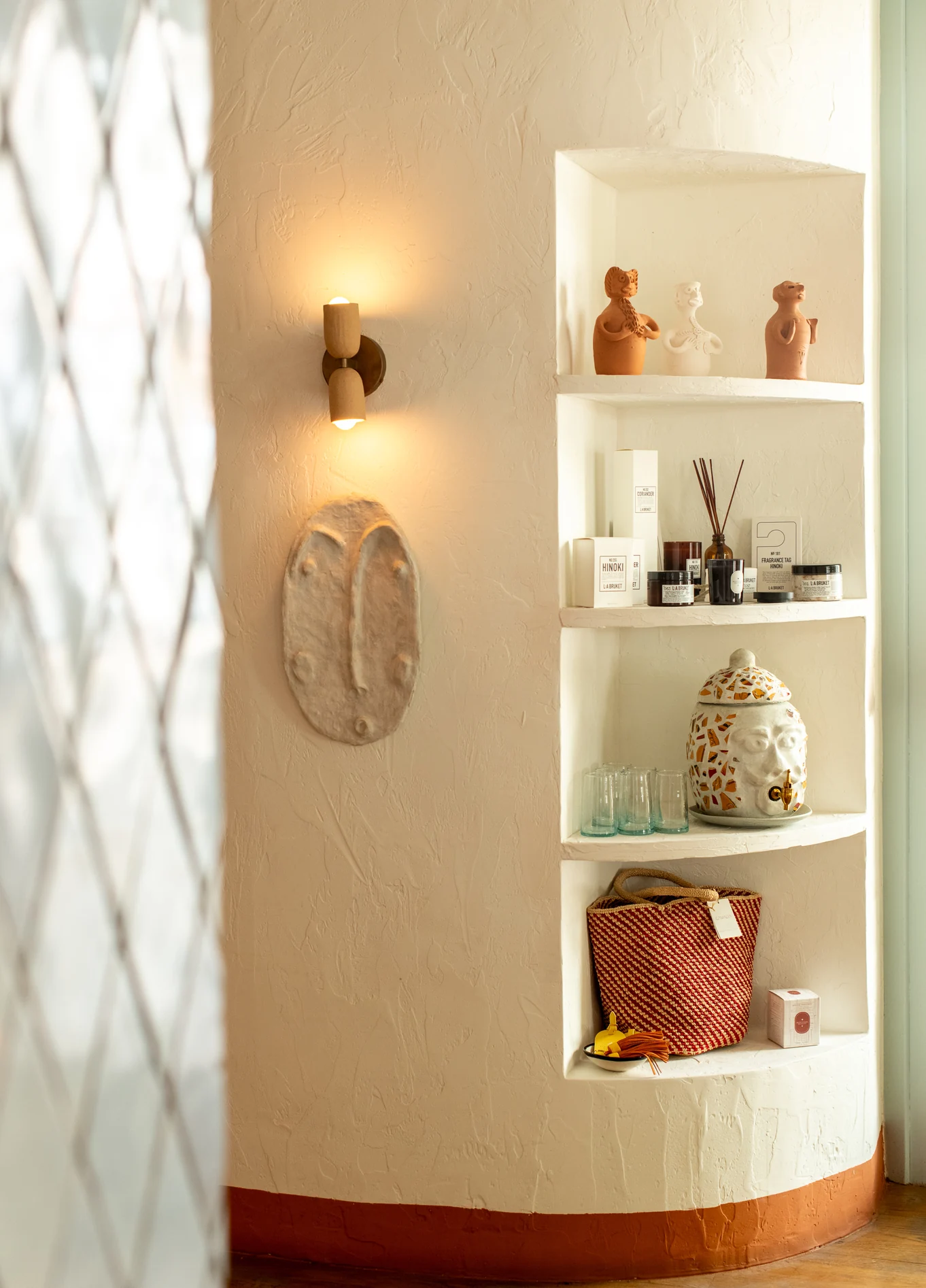 A curved, illuminated wall niche in a room at the Montesol Experimental hotel, containing decorative objects, with a wall lamp next to it.