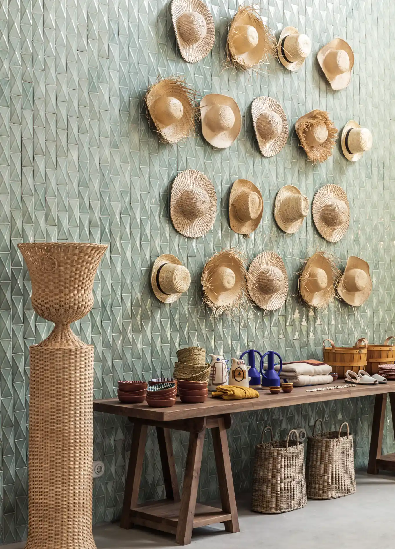 Wall decoration featuring straw hats on a green textured wall, accompanied by a long wooden table with various handcrafted items at Manorca Experimental.