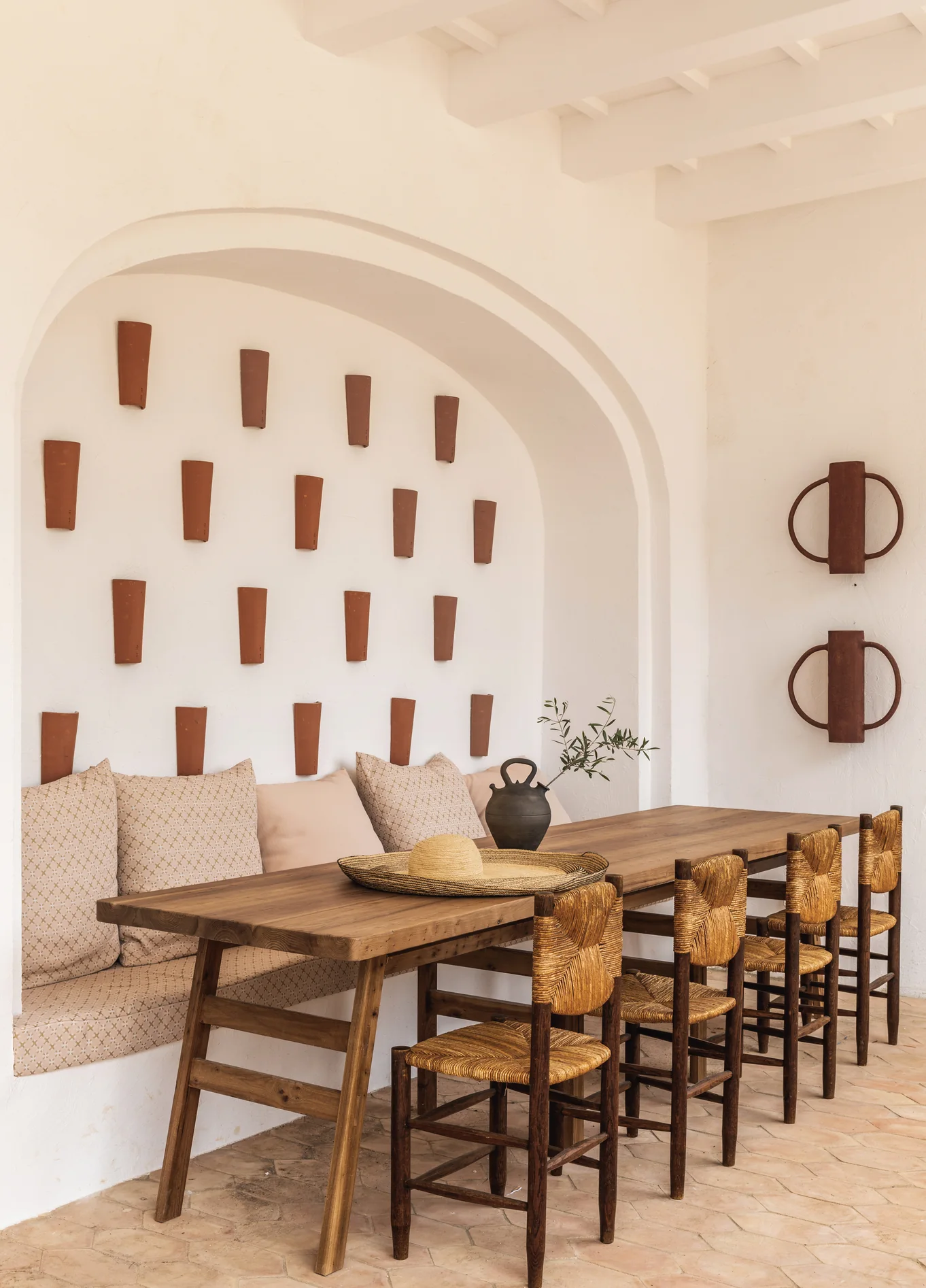 Overview of the dining space at Manorca Experimental, combining rustic design, comfortable banquettes, and artisanal wall decorations under an arch.