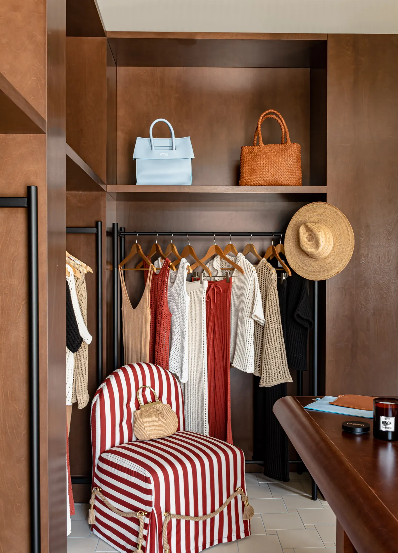 Elegant walk-in closet with hanging clothes, handbags on the top shelf, and a red and white striped armchair, creating a sophisticated atmosphere.