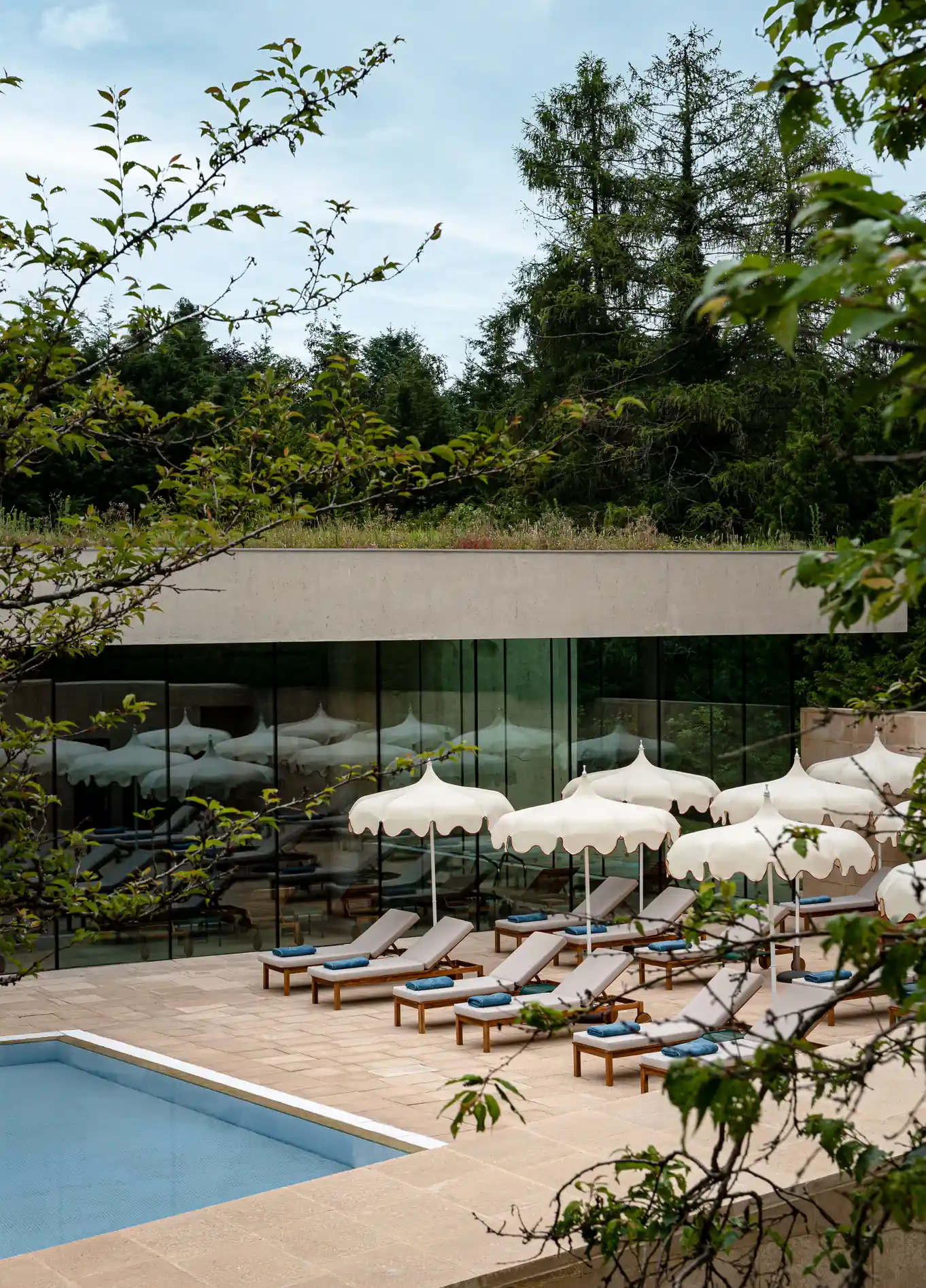 Outdoor swimming pool with sun loungers and parasols at Cowley Manor Spa Hotel, Cotswolds